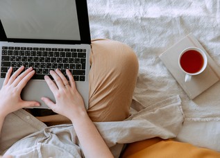 crop person using laptop with empty screen in bed near cup 3975580